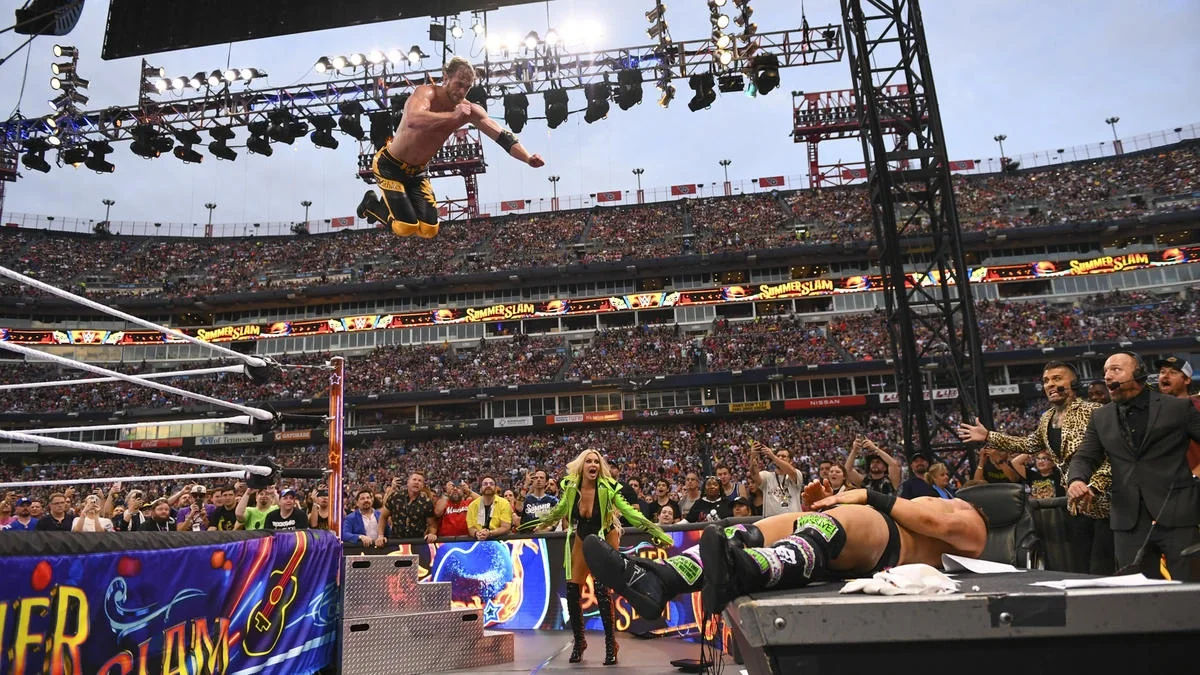 Logan Paul performing a frog splash from the top rope onto The Miz on the announce table